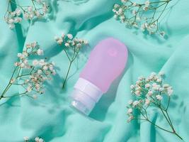 Pink plastic tube for cosmetics and sprigs of white gypsophila flowers, top view photo