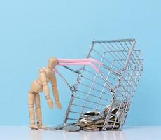 Wooden mannequin and loose change from a miniature shopping basket on a blue background photo