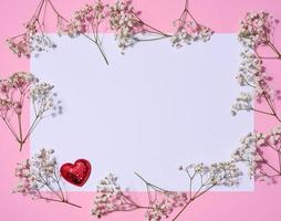 Empty white sheet of paper and gypsophilia flowers on a pink background, space for an inscription photo