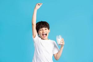 Portrait of asian boy holding cup of milk, isolated on blue background photo