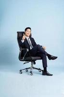 asiático empresario masculino retrato sentado en silla y aislado en azul antecedentes foto