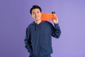 Image of young Asian man playing skateboard on purple background photo