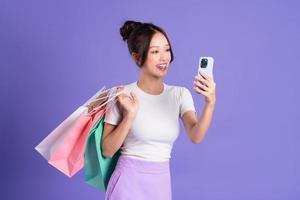 Young Asian woman holding shopping bag on purple background photo