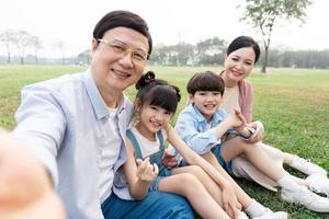 imagen de un asiático familia sentado juntos en el césped a el parque foto