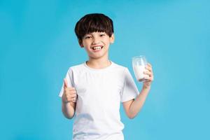 Portrait of asian boy holding cup of milk, isolated on blue background photo