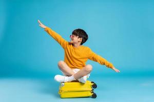 Asian boy pulling suitcase on blue background photo