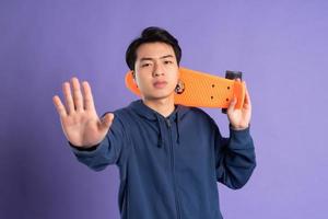 Image of young Asian man playing skateboard on purple background photo