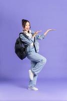 Portrait of a beautiful Asian schoolgirl wearing a backpack on a purple background photo