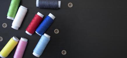 sewing threads and buttons on a dark wood background, spools of thread, multicolored threads, sewing accessories, top view photo