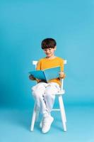 Portrait of sitting boy, isolated on blue background photo