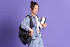 Portrait of a beautiful Asian schoolgirl wearing a backpack on a purple background photo