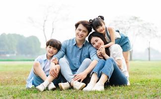 imagen de un asiático familia sentado juntos en el césped a el parque foto