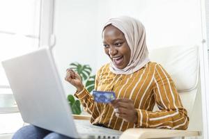 Elegant attractive Muslim woman using mobile laptop searching online shopping information in living room at home. Portrait of happy woman purchasing product via online shopping. Pay using credit card