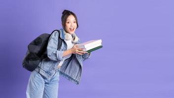 Portrait of a beautiful Asian schoolgirl wearing a backpack on a purple background photo