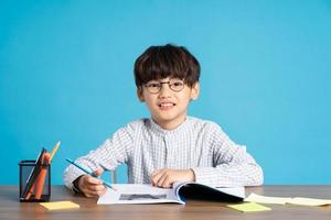 retrato de colegio chico sentado y estudiando en un azul antecedentes foto