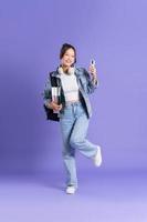 Portrait of a beautiful Asian schoolgirl wearing a backpack on a purple background photo