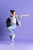 Portrait of a beautiful Asian schoolgirl wearing a backpack on a purple background photo