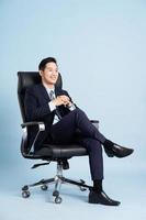 Asian businessman male portrait sitting on chair and isolated on blue background photo