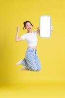 full body image of young Asian girl holding phone with cheerful face on yellow background photo