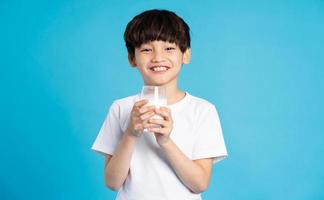 Portrait of asian boy holding cup of milk, isolated on blue background photo