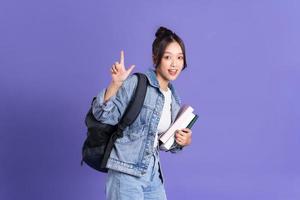 retrato de un hermosa asiático Chica de escuela vistiendo un mochila en un púrpura antecedentes foto