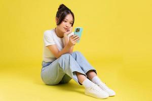 retrato de un hermosa joven asiático niña sentado en un amarillo antecedentes foto