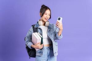 Portrait of a beautiful Asian schoolgirl wearing a backpack on a purple background photo