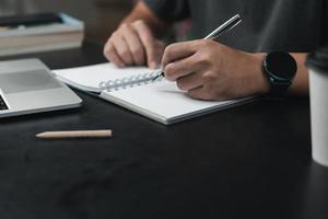 man hands with pen writing on notebook in the office.learning, education and work.writes goals, plans, make to do and wish list on desk. photo