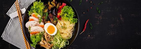 Japanese ramen soup with chicken, egg, shimeji mushrooms and eggplants on dark wooden background. Chanko nabe, sumo soup. Banner. Top view photo