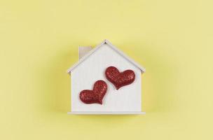 flat lay of wooden model house with two red glitter hearts on yellow  background. dream house , home of love, strong relationship, valentines. photo