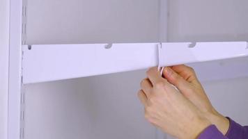 Installation brackets of a metal mesh shelf in the dressing room system on a bracket. Hands is assembling a white holder storage system close-up video