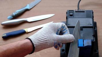 Sharpening a knife on an electric sharpener at home. The man's hand drives the knife blade between the blue sharpeners, dust flies on the machine. 4k, slow motion video