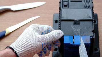 verscherping een mes Aan een elektrisch slijper Bij huis. de man's hand- schijven de mes blad tussen de blauw slijpers, stof vliegt Aan de machine. 4k, langzaam beweging video