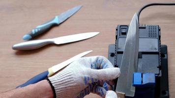 Sharpening a knife on an electric sharpener at home. The man's hand drives the knife blade between the blue sharpeners, dust flies on the machine. 4k, slow motion video