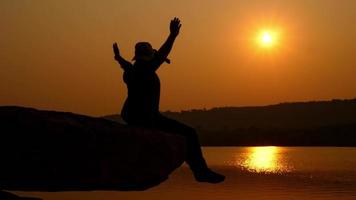 Tourist sitting on rocky cliff near river at sunset video