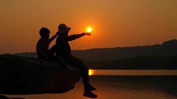 toerist zittend Aan rotsachtig klif in de buurt rivier- Bij zonsondergang video