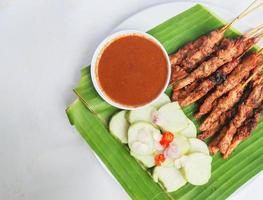 chicken satay or chicken satay served with lontong, rice cake and peanut sauce. served on banana leave photo