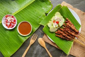 chicken satay or chicken satay served with lontong, rice cake and peanut sauce. served on banana leave photo