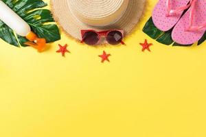 Beach accessories with straw hat, sunscreen bottle and seastar on yellow background top view with copy space photo