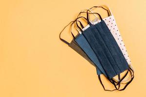 Top view of a pile of homemade textile reusable masks on orange background. Respiratory protection concept with copy space. DIY concept photo