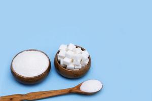 crystal white sugar, lump sugar in wooden bowls and wooden spoon on blue background with copy space photo