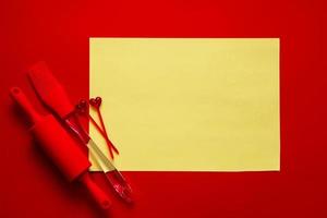 silicone red culinary accessories on red background with blank yellow sheet, mockup photo