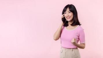 Pretty young asian woman showing success, victory hand gesture while receiving great news from smartphone on pink background. Happy technology, mobile phone advertisement, online application concept photo