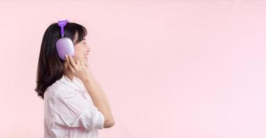 Side view young smiling cheerful fun woman she wear pink shirt white t-shirt headphones listen to music use mobile cell phone isolated on plain pastel light pink background. People lifestyle concept. photo