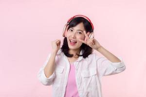 Smile pretty asian model person listen music song and enjoy dance with wireless headphone online audio radio sound. Positive fun exited joyful youth female woman on pink isolated background studio photo