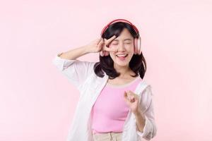sonrisa bonito asiático modelo persona escucha música canción y disfrutar danza con inalámbrico auricular en línea audio radio sonido. positivo divertido salido alegre juventud hembra mujer en rosado aislado antecedentes estudio
