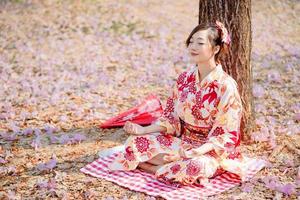 asiático mujer en tradicional kimono vestir practicas meditación a Cereza florecer árbol. foto
