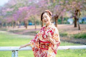 Happy young woman in traditional kimono dress holding dango at bridge in spring festival. Emotion smile photo
