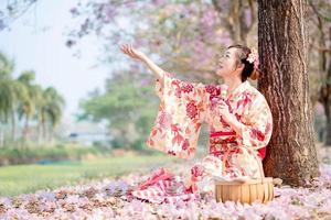 Spring festival. Young lady in traditional kimono dress sitting and holding dango at cherry blossom tree. photo