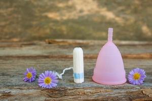 Menstrual cup and tampons on old wooden background. photo